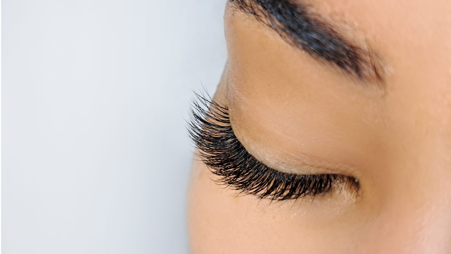 Closed eye with long, dark eyelashes against soft blue background