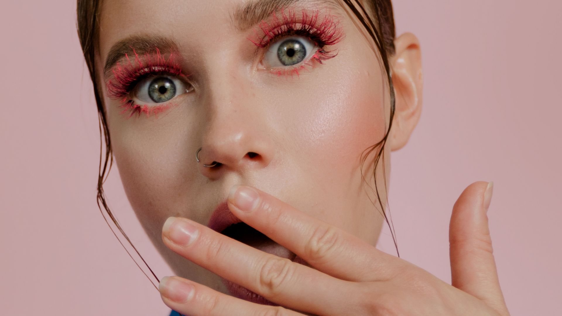 Close-up of person with bright pink eyeshadow and nose ring touching lips