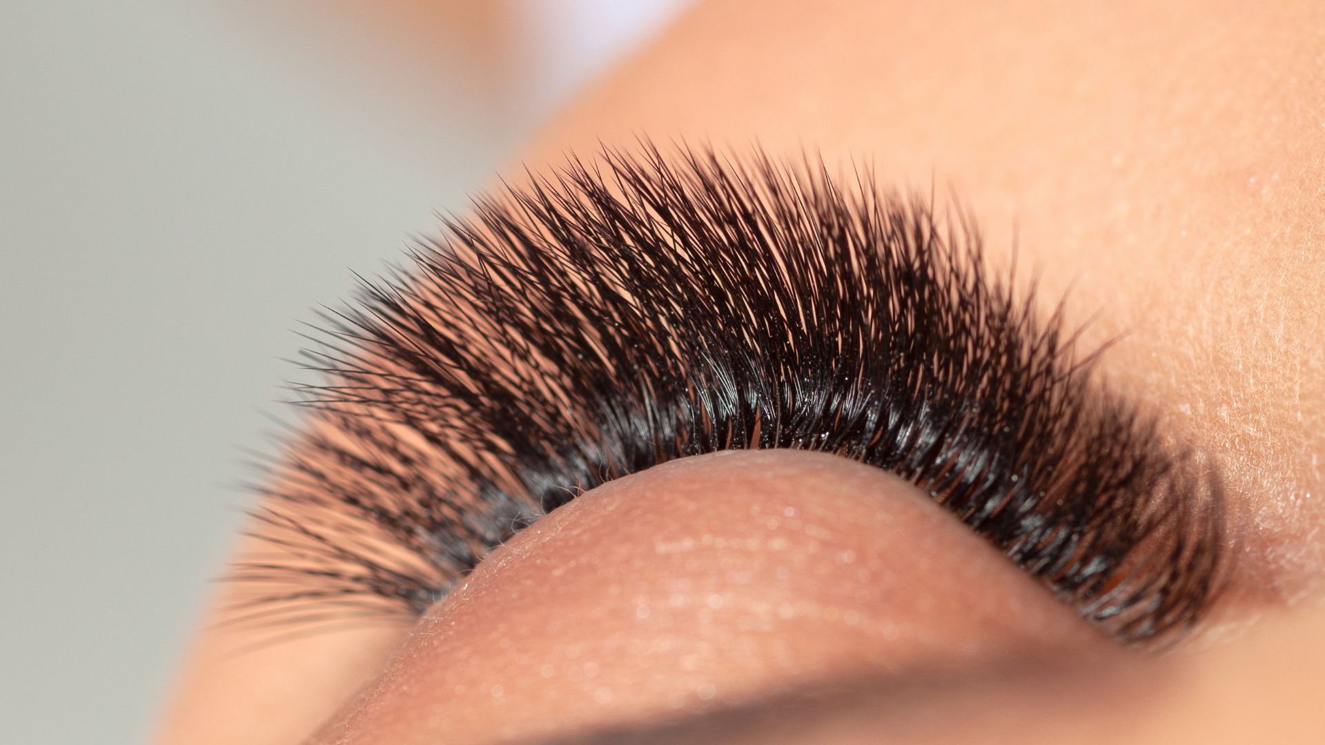 Macro close-up of long, dark eyelash with soft peach-toned background