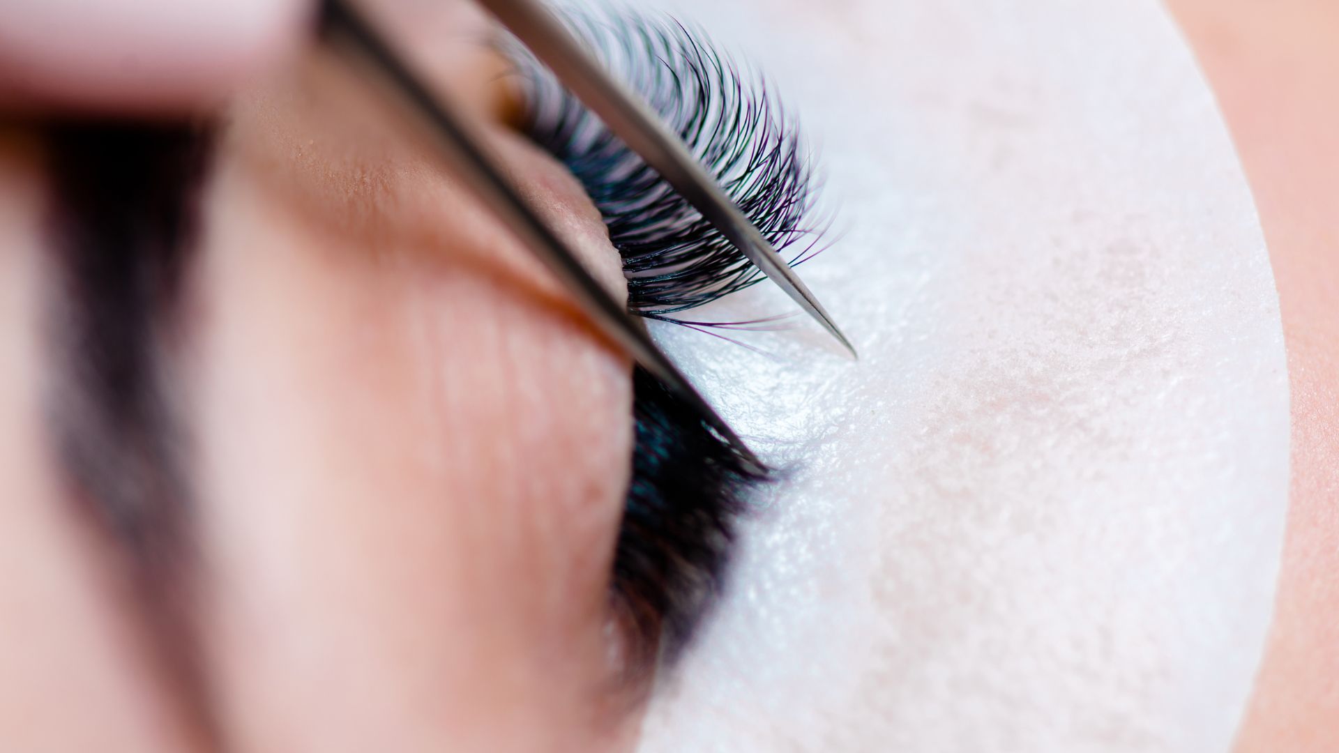 Close-up of eyelash extension application with precision tweezers