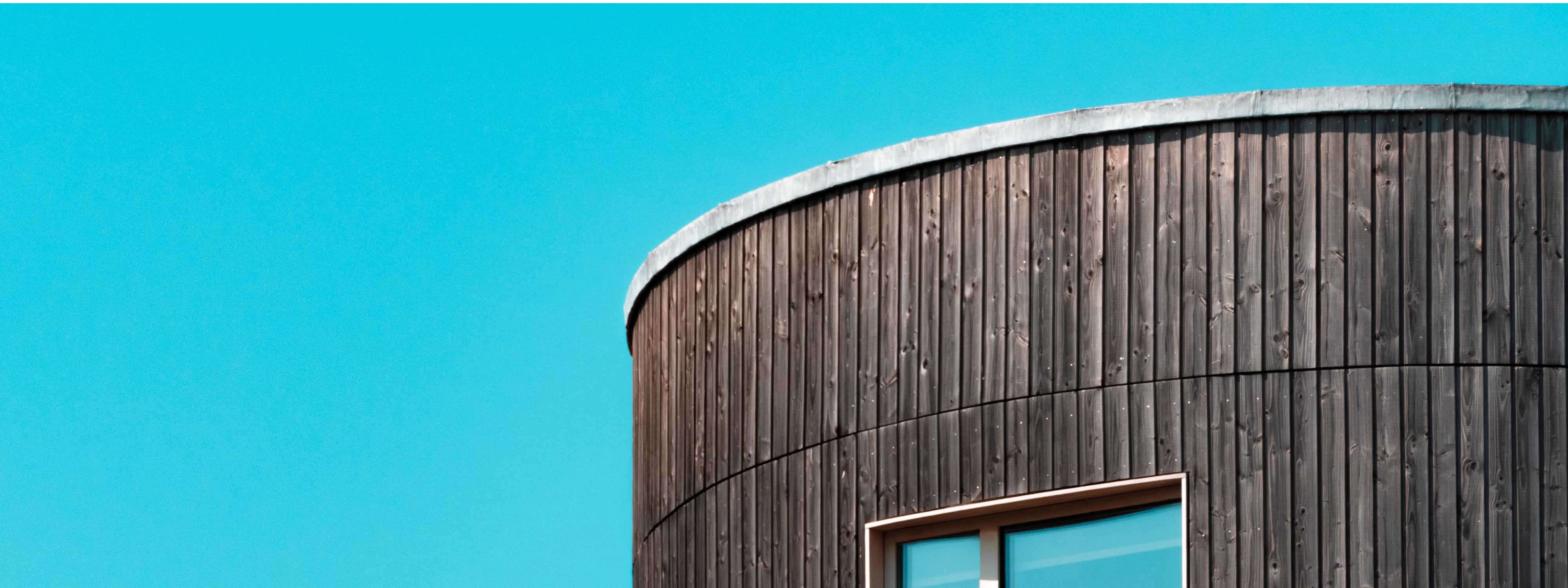 Curved wooden building exterior with window against bright turquoise background